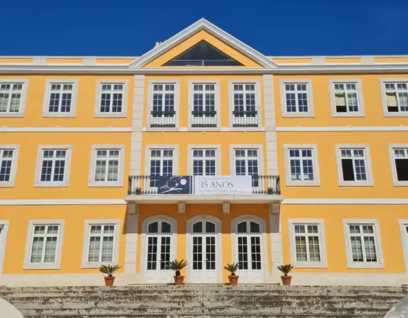 Fachada da sede da Fundação Cidade de Lisboa, edifício amarelo de três andares com estilo clássico e bandeira comemorativa dos 35 anos.